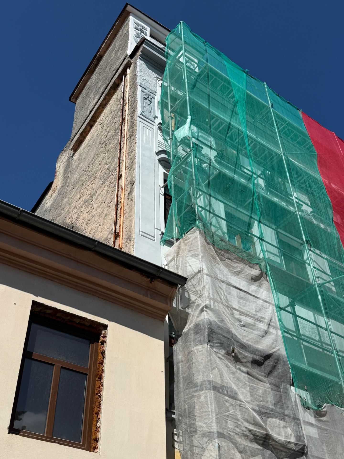 Činžovní dům v České Lípě v průběhu renovace fasády — lešení se zelenou sítí a rozpracovaný nároží